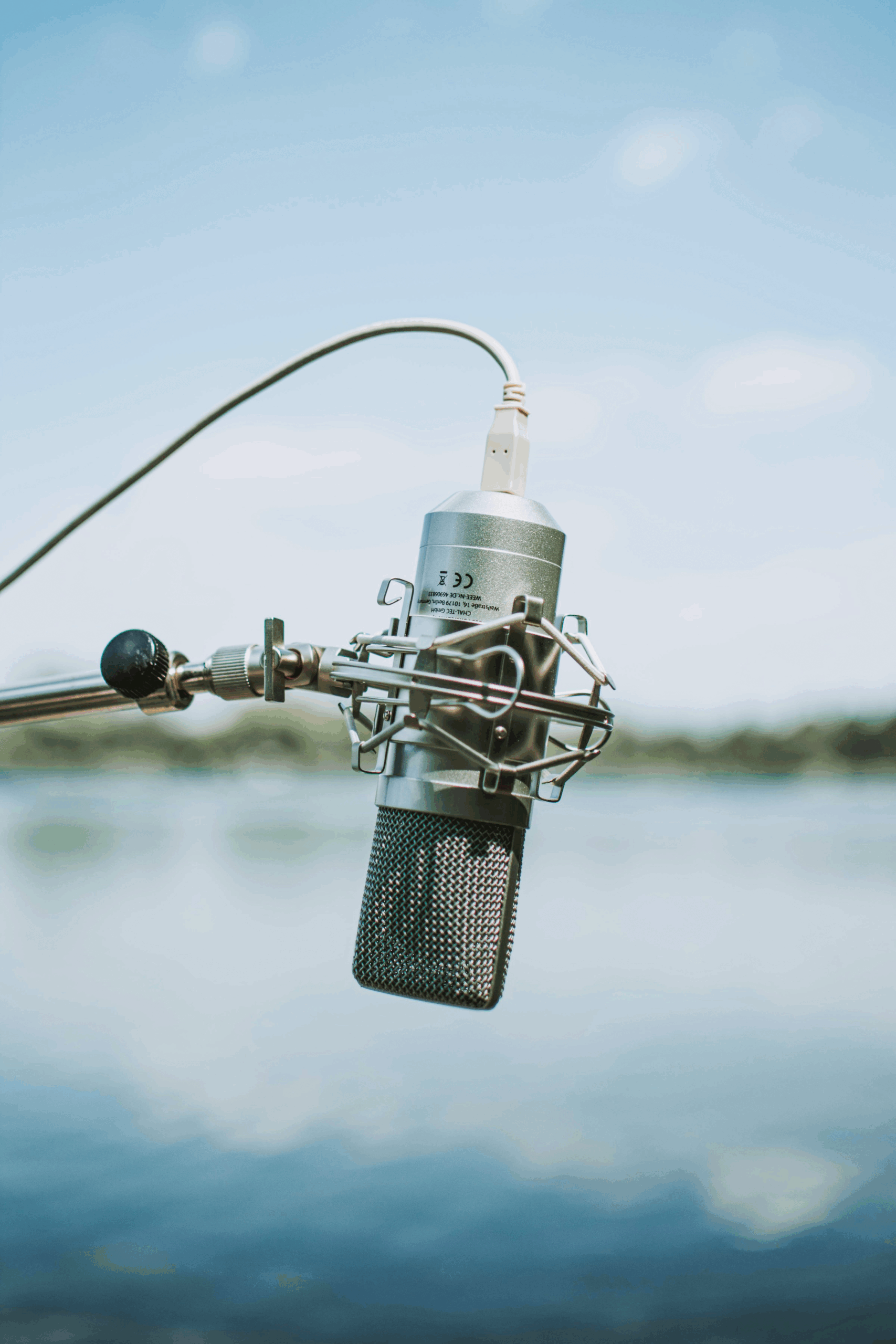 Microphone on a stand with a serene waterfront background, highlighting its use for recording or broadcasting in an outdoor setting.